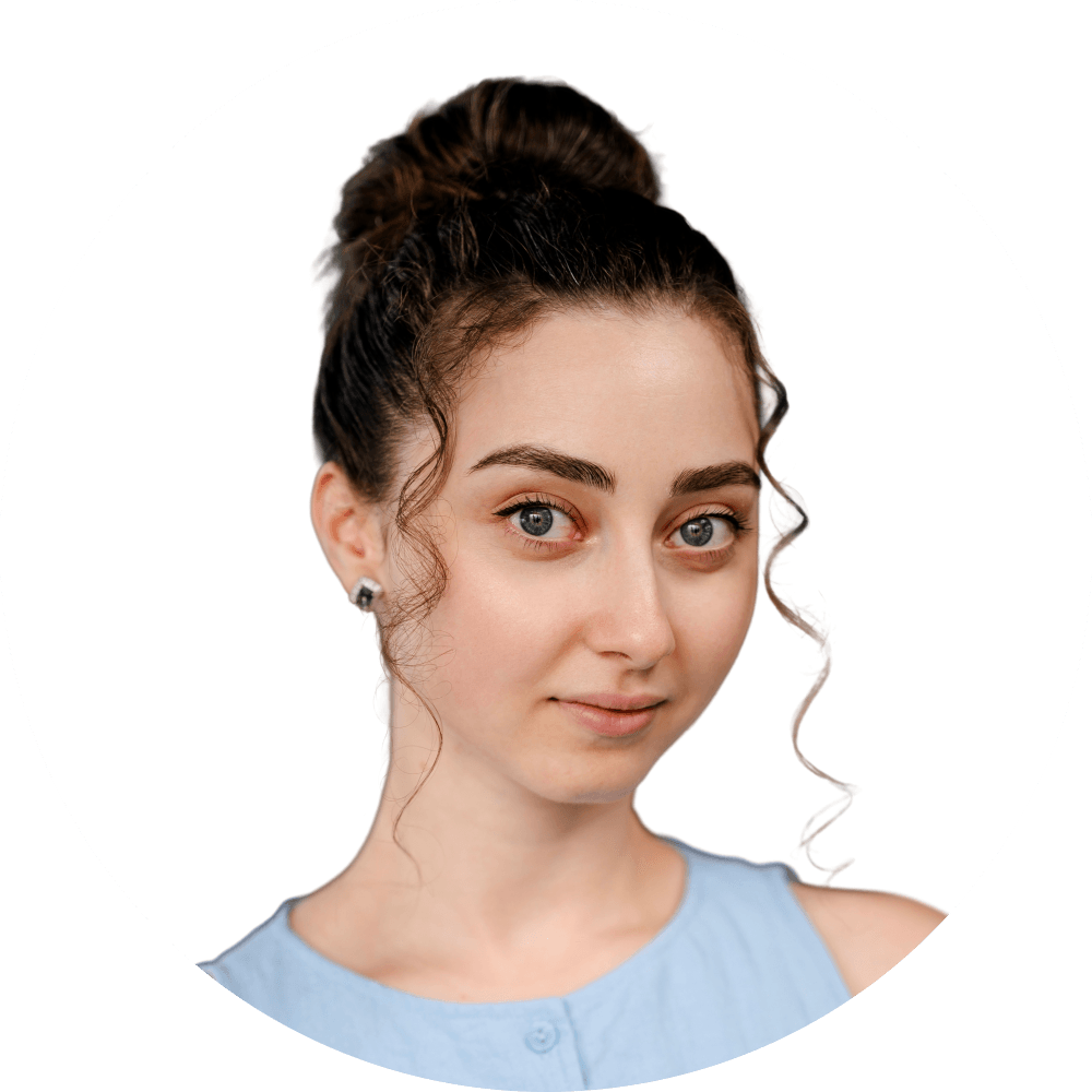 Young woman with dark hair bun and light blue top looks directly at camera.