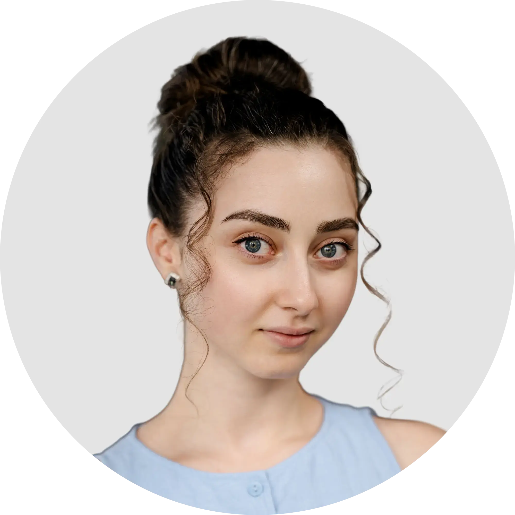 Young woman with dark hair in a bun, wearing a light blue top, looking forward.