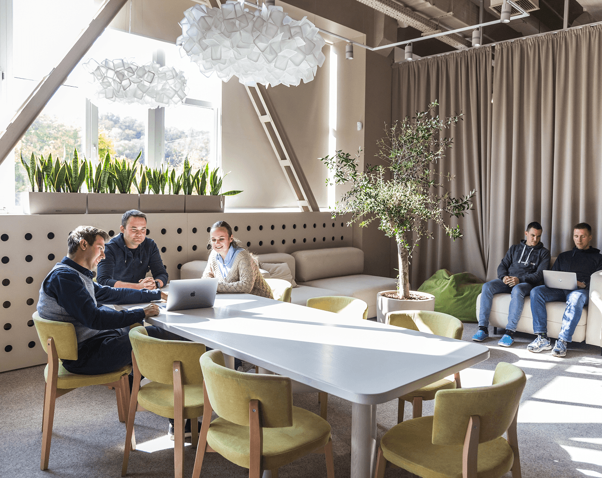 Coworkers collaborate at a table in a modern office, while others relax on a sofa.
